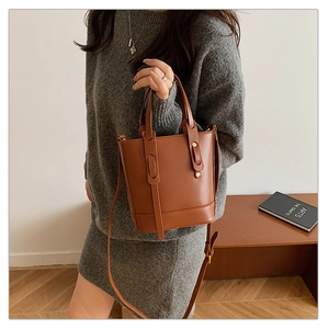 Detail of brown leather bucket bag featuring gold rivets and dual handles in a cozy room