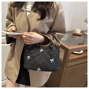 Detail of black quilted handbag with white bow embroidery and brown handle contrast