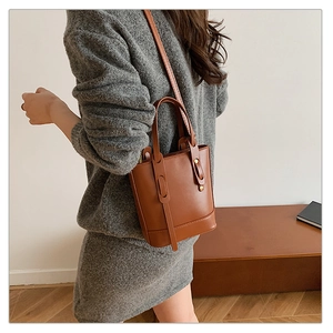 Detail of a brown PU leather bucket bag with top handles and gold hardware details