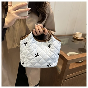 Detail of light blue quilted tote with black bow embroidery and brown leather trim