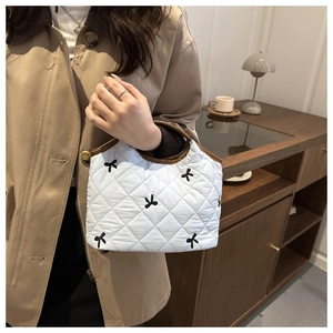 Quilted white handbag with black bow embroidery shown in a cozy lifestyle setting