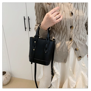 Close-up of black PU bucket bag worn over shoulder with beige cardigan and gold hardware