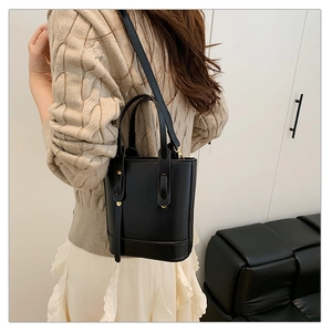 Side view of black faux leather bucket bag with gold rivets on clean indoor background