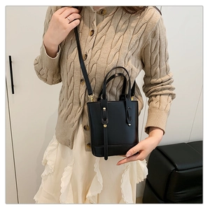 Detail of a minimalist black leather bucket bag with gold hardware and a long strap
