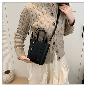 Chic black bucket bag with gold rivets and detachable strap shown on model's shoulder