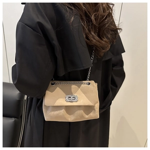 Sac bandoulière beige chic avec chaîne argentée porté sur un trench-coat noir