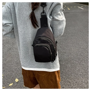 Outdoor shot of a black minimalist nylon crossbody bag worn over a grey sweatshirt