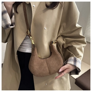 Detail of a brown suede crescent bag featuring golden hardware and adjustable strap