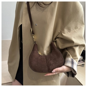 Close-up of a vintage dark brown suede half-moon crossbody bag with gold metal hardware