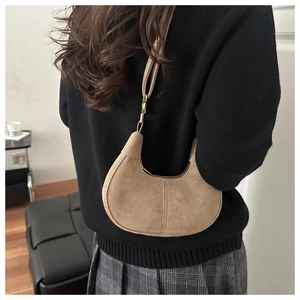 Close-up of a minimalist suede hobo bag in camel color worn by a model in a casual setting