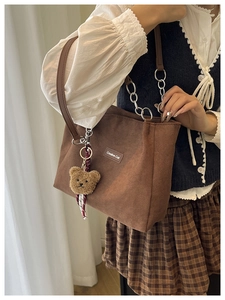 Détail d'un sac cabas en daim marron avec étiquette Creative Cat et breloque ours en peluche