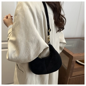 Detail view of black suede crescent bag featuring high-quality gold hardware and straps