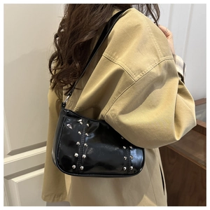 Close-up of black patent leather underarm bag with silver rivet details and strap