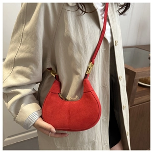 Detail of red suede half-moon bag with gold buckle on a model wearing a beige coat