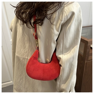 Detailed close-up of a red suede crescent bag worn by a model in a minimalist setting