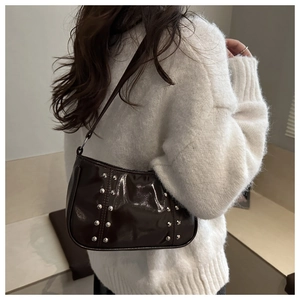 Détail du sac sous les aisselles marron brillant avec rivets argentés sur pull blanc