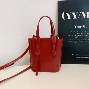 Sac seau rouge minimaliste avec poignées et bandoulière réglable dans un studio moderne