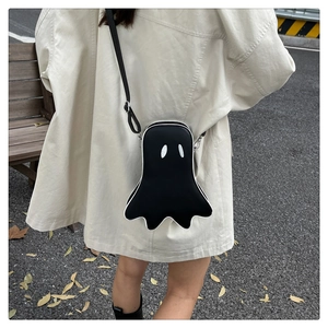 Outdoor view of a black ghost-shaped crossbody bag with white eyes and adjustable strap