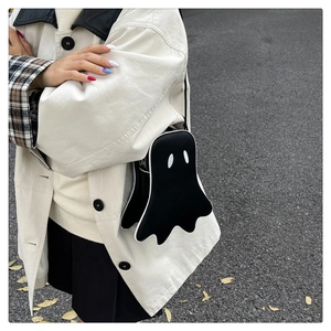 Close-up of a cute ghost-shaped crossbody bag worn over a beige trench coat outdoors