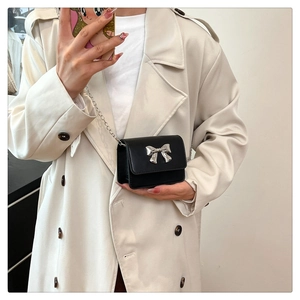 Detail shot of black leather mini flap bag featuring silver bow clasp and fine chain strap