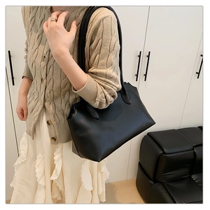 Minimalist black leather tote bag shown on shoulder in a modern home lifestyle setting