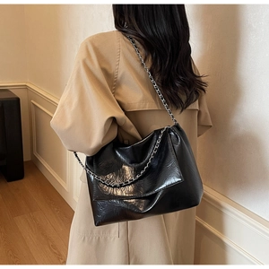 Detailed view of black tote bag with glossy wrinkled texture and silver chain strap