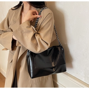 Detail of glossy black patent leather shoulder bag with chain strap on a trench coat