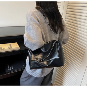 Detail of black glossy wrinkled texture tote bag with chain strap and flap closure
