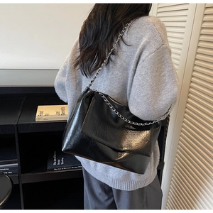 Detailansicht einer schwarzen Lackleder-Tote-Bag mit silberner Kette an einem Modell