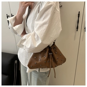 Close-up of brown leather bucket bag featuring silver rivet studs and drawstring closure