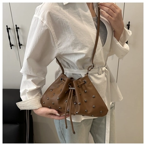 Brown bucket bag with silver studs and drawstring closure shown on shoulder
