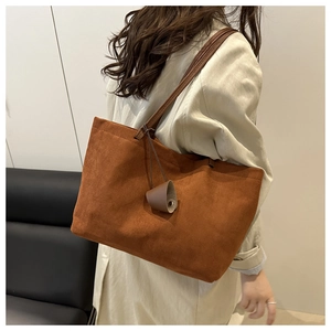 Close-up of brown suede tote bag featuring slim shoulder strap and stylish charm