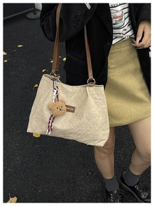 Détail du sac cabas en toile beige matelassé avec pendentif ours et bandoulière marron