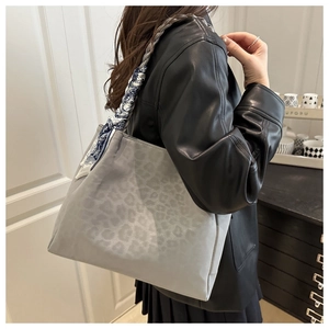 Detail of grey leopard embossed tote bag with a patterned silk scarf on a braided handle