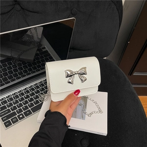 White mini crossbody bag with silver butterfly buckle and chain strap on desk