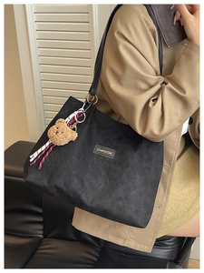 Dettaglio della borsa shopper nera rétro con ciondolo a orsetto e texture elegante.