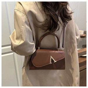 Detail view of brown leather crossbody bag with gold V hardware on khaki trench coat