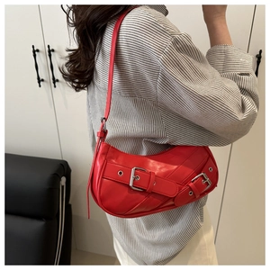 Model wearing a red biker-style underarm bag with decorative metal buckle and long strap