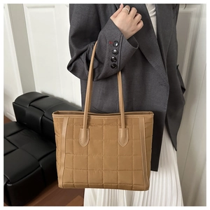 Quilted khaki tote bag in glossy nylon shown on shoulder with gray blazer and white skirt