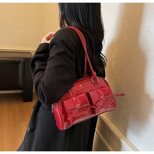 Vue latérale d'un sac à épaule en cuir verni rouge avec nœuds décoratifs sur un modèle