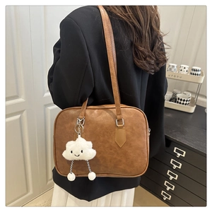Detail of a brown leather bowling bag with a cute white plush cloud charm on a strap