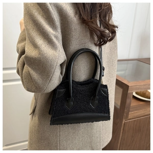 Detail of black faux fur crossbody bag with leather trim on model in grey blazer