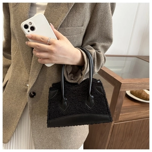 Detail of black faux shearling handbag with leather base held in a city cafe setting