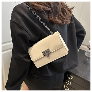Detailed view of beige crossbody bag with black metal chain strap and vintage buckle