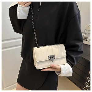 Detail of minimalist cream chain crossbody bag with metallic geometric lock and rivet accents