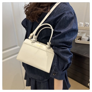 Detail of a creamy white crossbody bag with a twist ring handle and gold fashion lettering