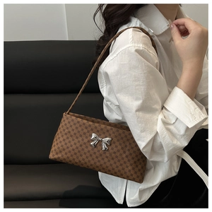 On-shoulder view of a brown vintage tote bag with geometric print and silver bow detail