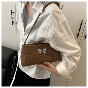 Detail of a brown printed shoulder bag with a metallic 3D bow on a white shirt model