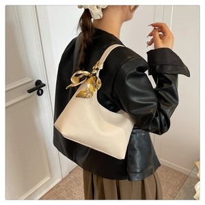 Detail of a beige lychee texture leather hobo bag with a patterned silk scarf on strap