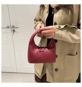 Detail of burgundy crescent leather handbag with integrated handle and top zipper